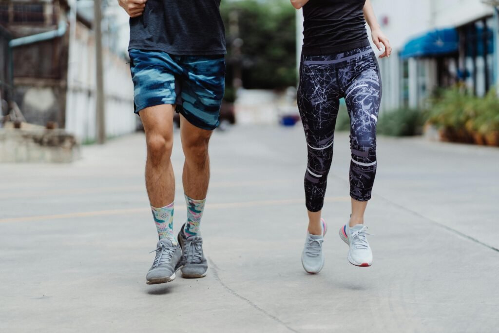 A fit couple jogging outdoors, showcasing vibrant activewear and sneakers in an urban setting.