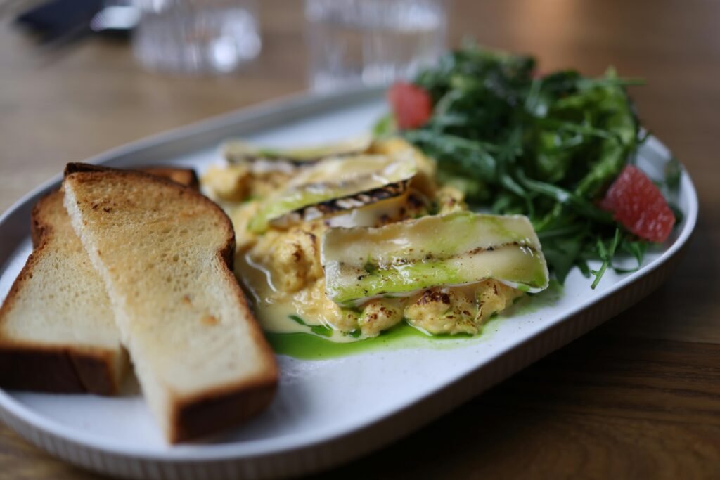 Delicious breakfast plate with cheesy scrambled eggs, toast, and fresh salad on a wooden table.