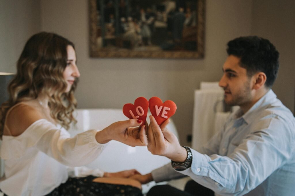 A couple sharing a romantic moment indoors, holding heart-shaped love symbols, enhancing a Valentine's Day feel.